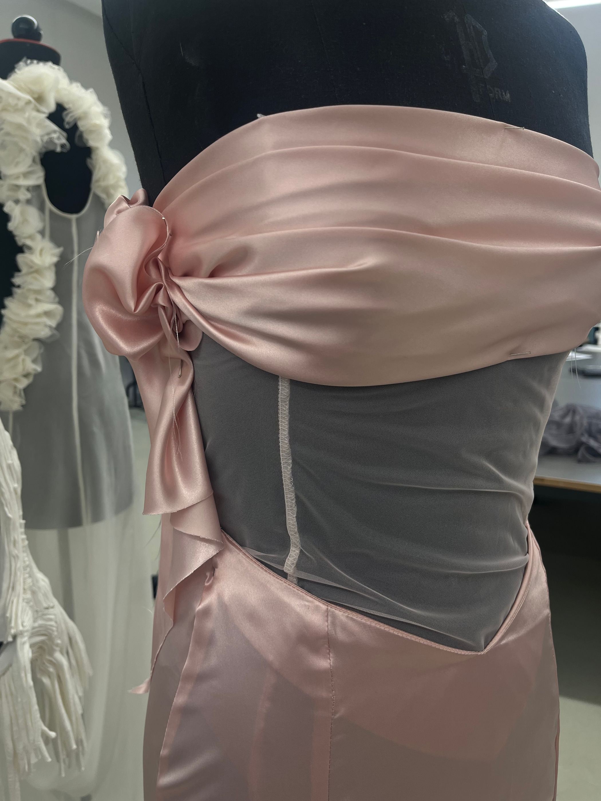 Detail am Kleiderständer: rosa Satinschärpe über transparentem Mesh-Korsett.
