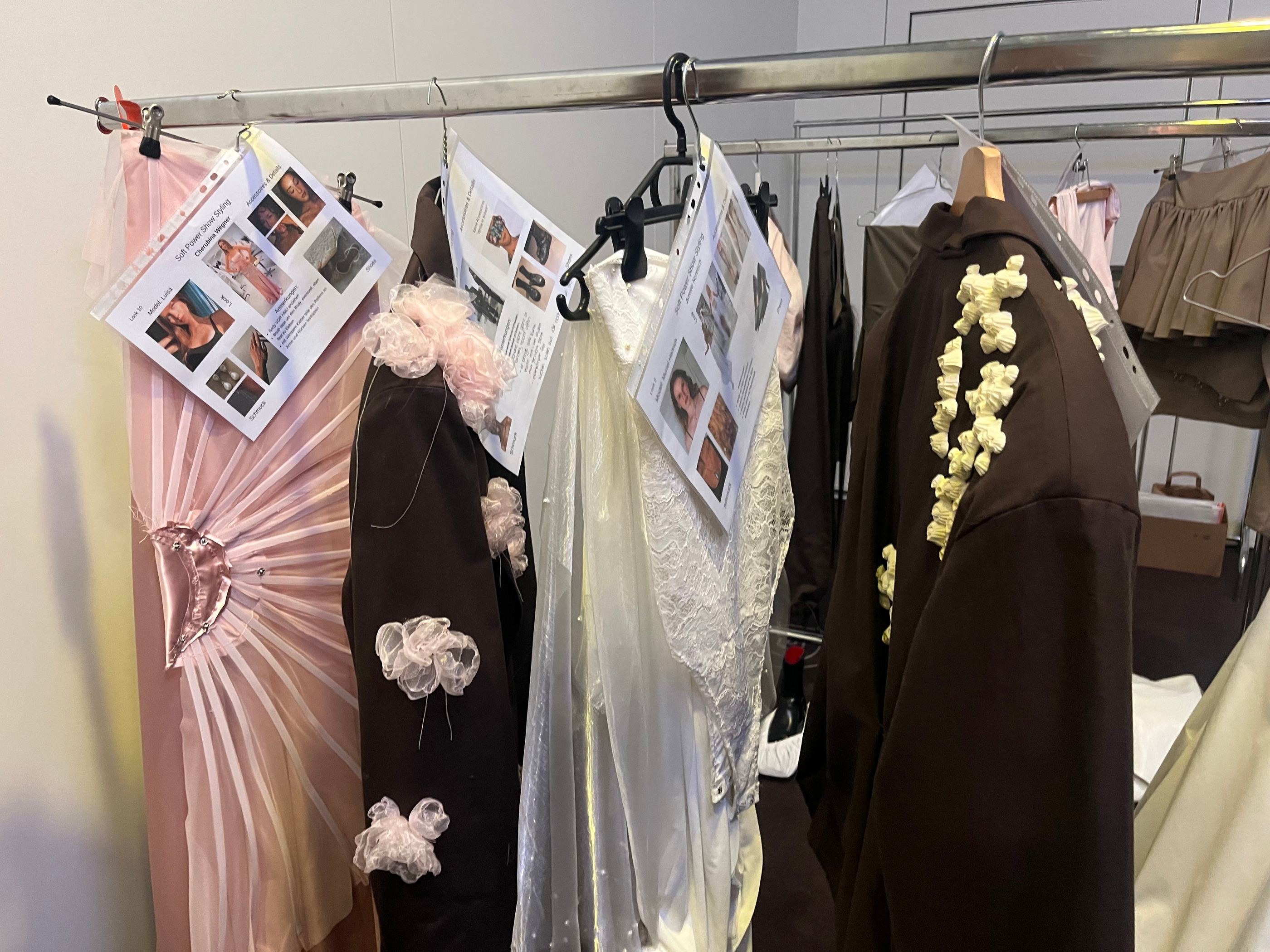 Kleiderstange backstage: an jedem Look hängt ein ausgedrucktes Styling-Blatt mit Bildern und Notizen.
