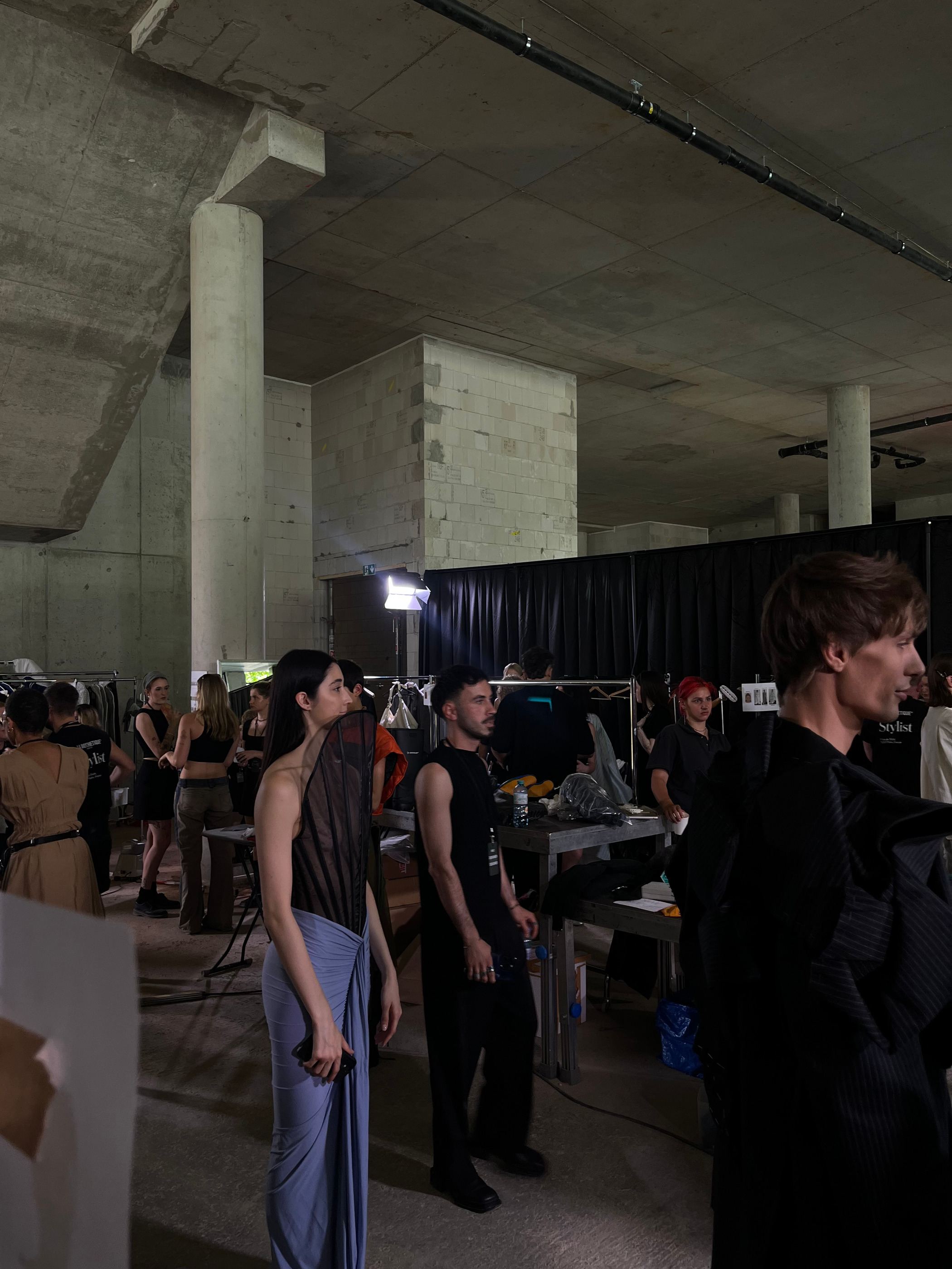 Blick über eine Betontreppe auf einen Backstagebereich mit Schminktischen und wartenden Models.
