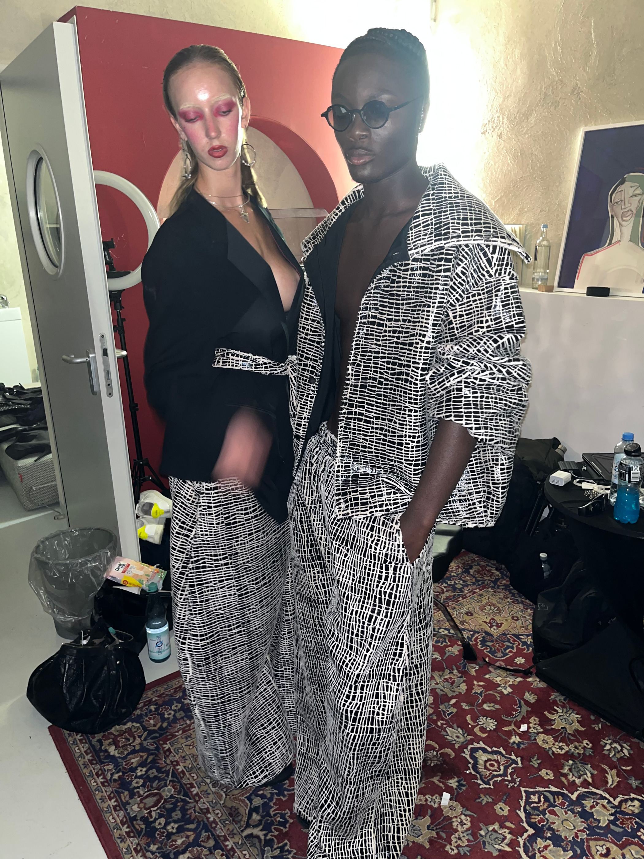 Zwei Models in schwarzen und schwarzweiß gemusterten Looks im Ankleidebereich.